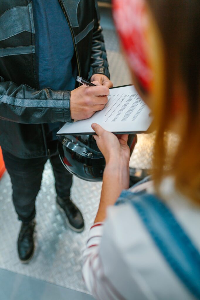 Biker man signing insurance policy on workshop while female mechanic holding clipboard