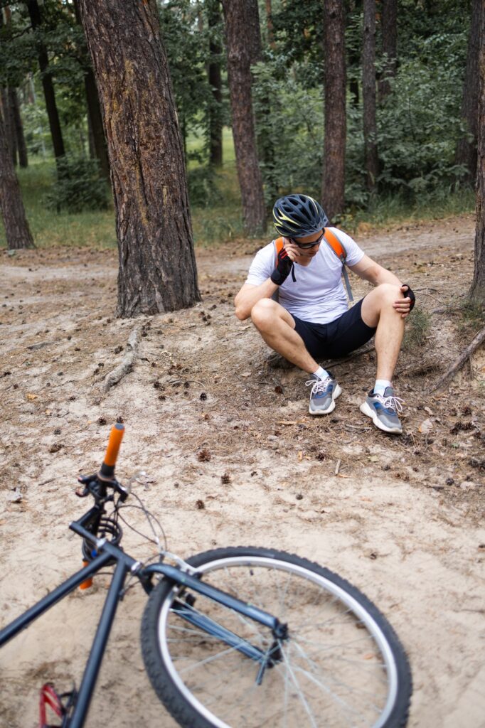 Man fallen off his bike in park. Bicycle accident. Biker lying on the road and holding his leg.