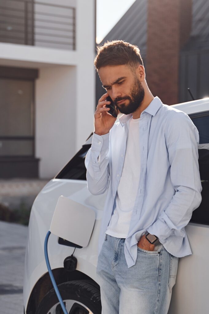 Talking by the phone. Young stylish man is with electric car at daytime