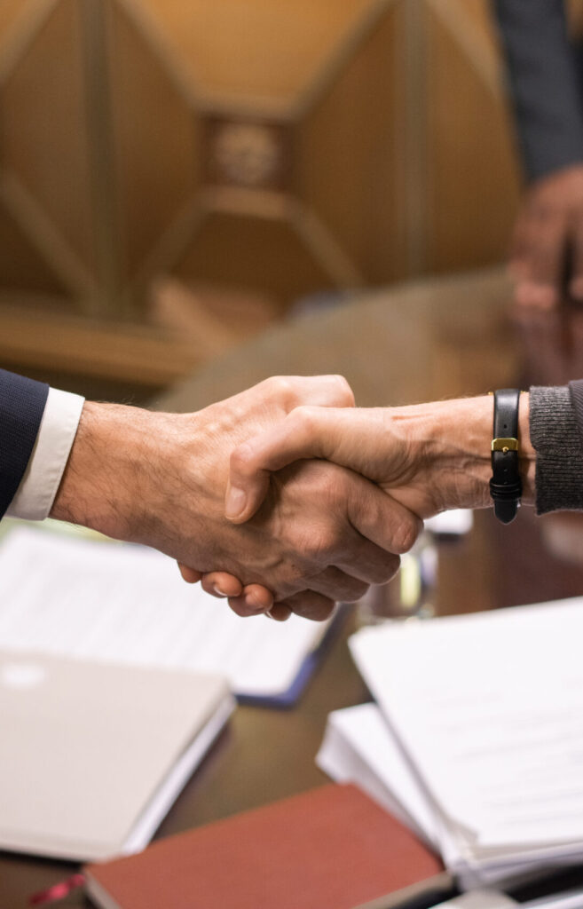 Hände zweier erfolgreicher Geschäftspartner beim Händeschütteln über einem Tisch mit Dokumenten