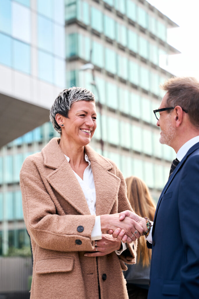 Fröhlich lächelndes Team verschiedener Geschäftsleute in formellen Anzügen, die selbstbewusst in die Kamera schauen