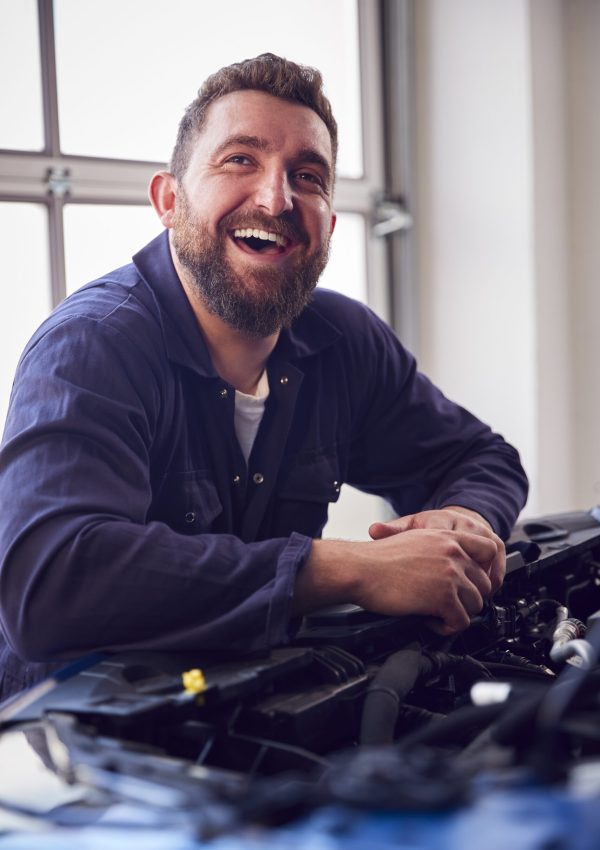 Mechaniker in der Garage schaut unter die Motorhaube des Autos, während er den Motor wartet