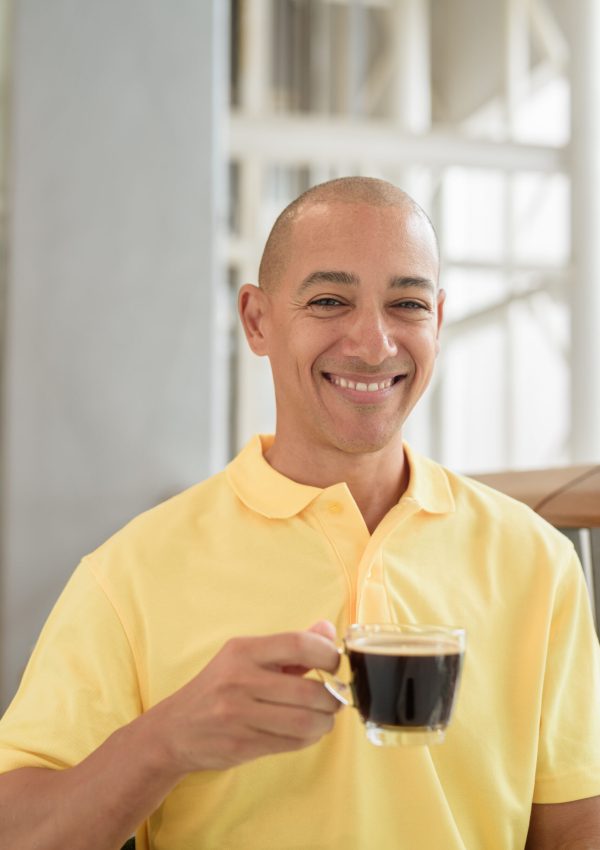 Reifer hispanischer glatzköpfiger Mann sitzt in einem Café und hält eine Kaffeetasse