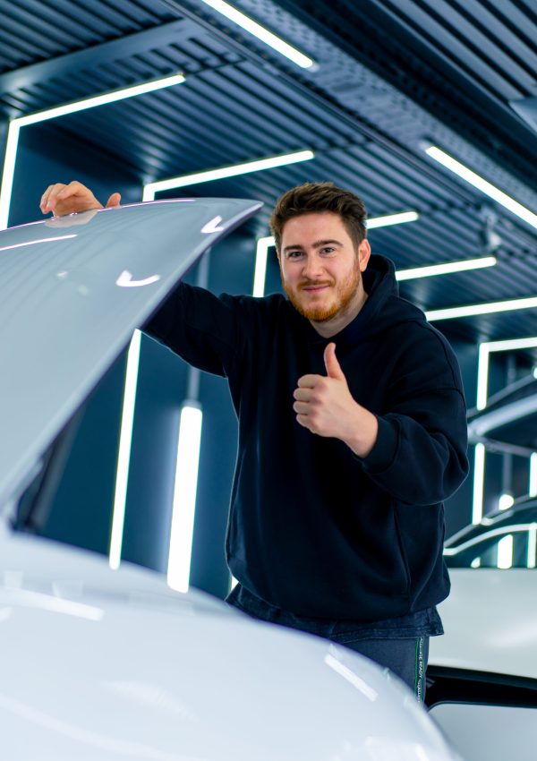 Porträt eines Mannes, der sich freut und Daumenzeichen zeigt, weil sein weißes Luxusauto repariert wurde